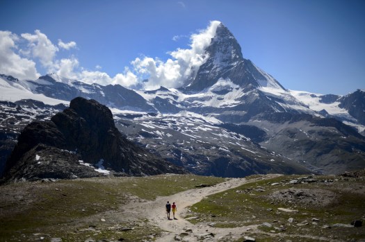 A couple of tourists walk on a trail below the Matterhorn mountain in Zermatt on June 30, 2015. The resort celebrates this year the 150th anniversary of the iconic Alpine mountain's first climb. AFP PHOTO / FABRICE COFFRINI (Photo credit should read FABRICE COFFRINI/AFP/Getty Images)